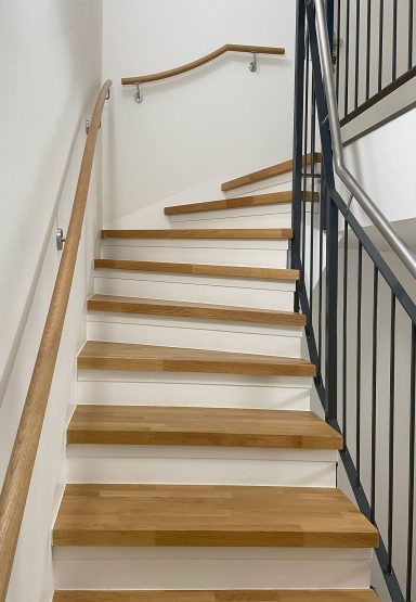 Helle Treppe mit Eichenstufen, weiß lackierten Seitenwangen und Metallgeländer. An der Wand ein passender Handlauf aus Eiche Vollholz.